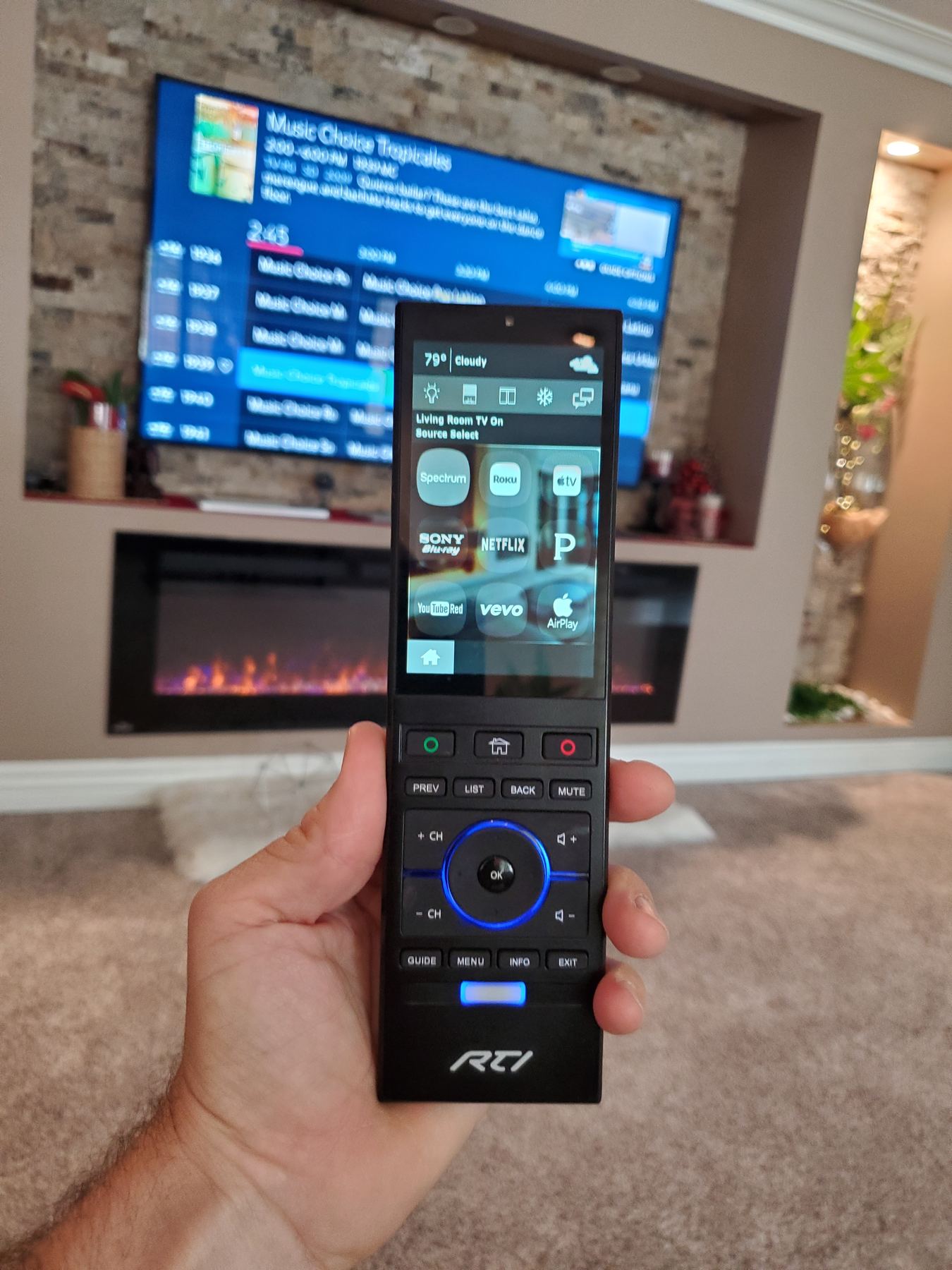 RTI remote showing a music screen in front of a TV and fireplace