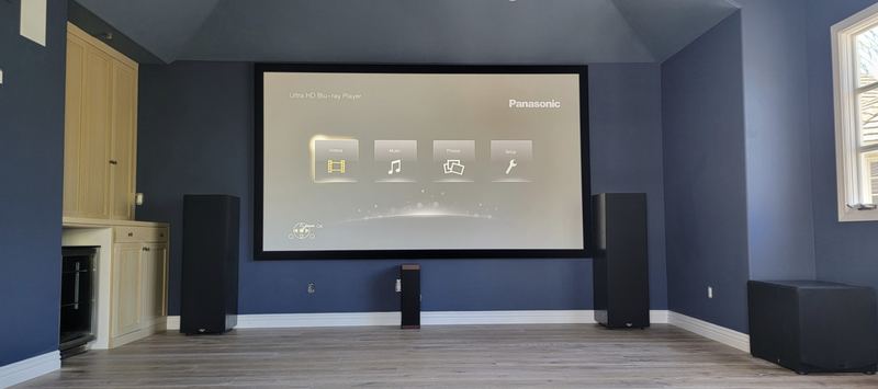 Dedicated home theater with a large fixed-frame projection screen, tower speakers, center channel and subwoofer in a blue media room