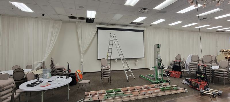 200-inch projection screen being installed on the front wall of a banquet hall, with a ladder and lift on site